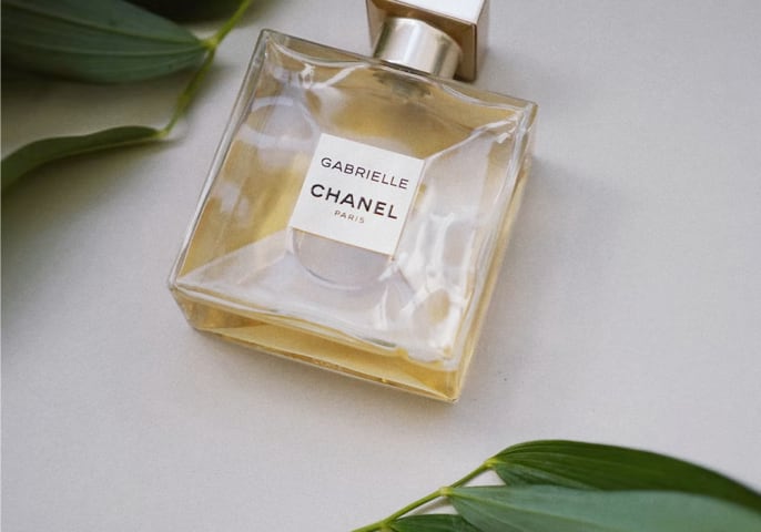 bottle of Gabrielle CHANEL perfume laying on the table with two green leaves around it