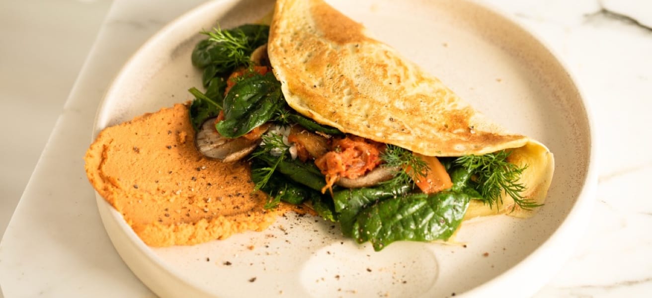 a photo of an omelette with vegetables inside laying on a white plate